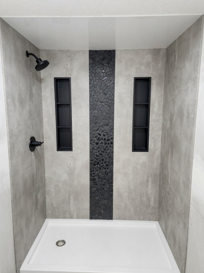 Walk-in shower with concrete-look walls, river pebble stripe, and dual black niches