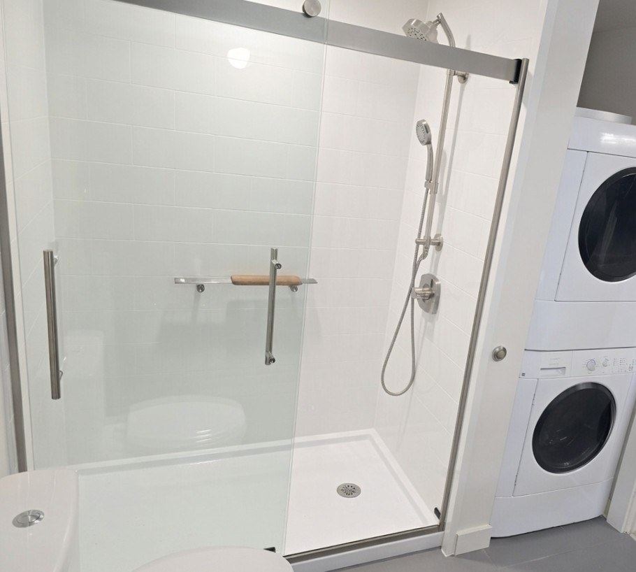 Walk-in shower with sliding glass doors next to stacked washer and dryer