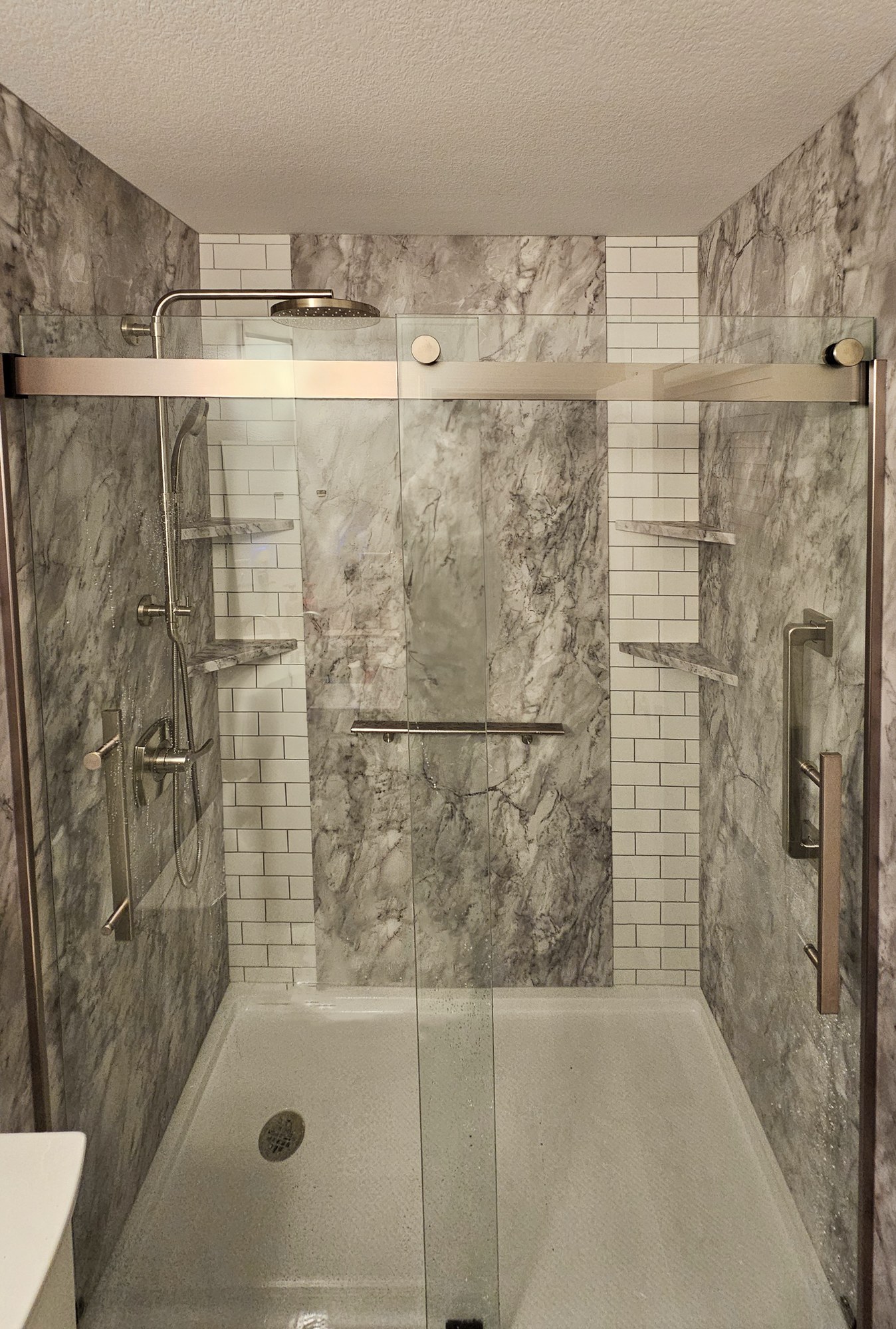 Marble-look walk-in shower with subway tile strips, grab bars, and sliding glass doors