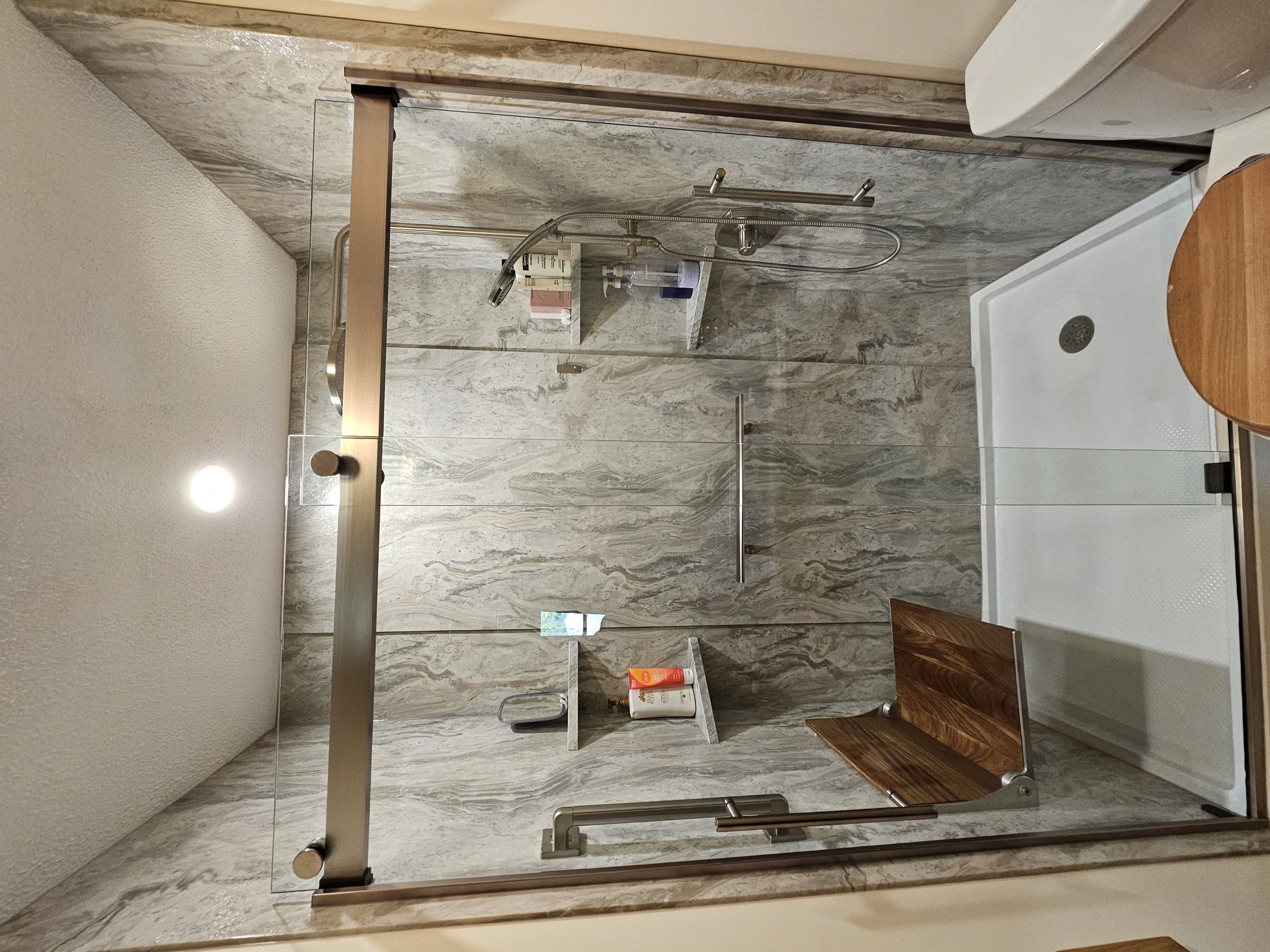 Marble-look walk-in shower with sliding glass doors and teak fold-down seat